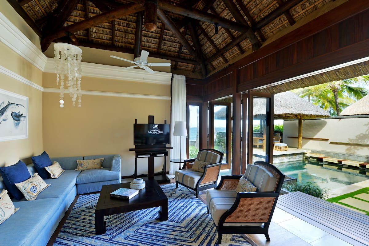 Una sala de estar con sofá, sillas, una mesa de centro, televisor y vista a una piscina.