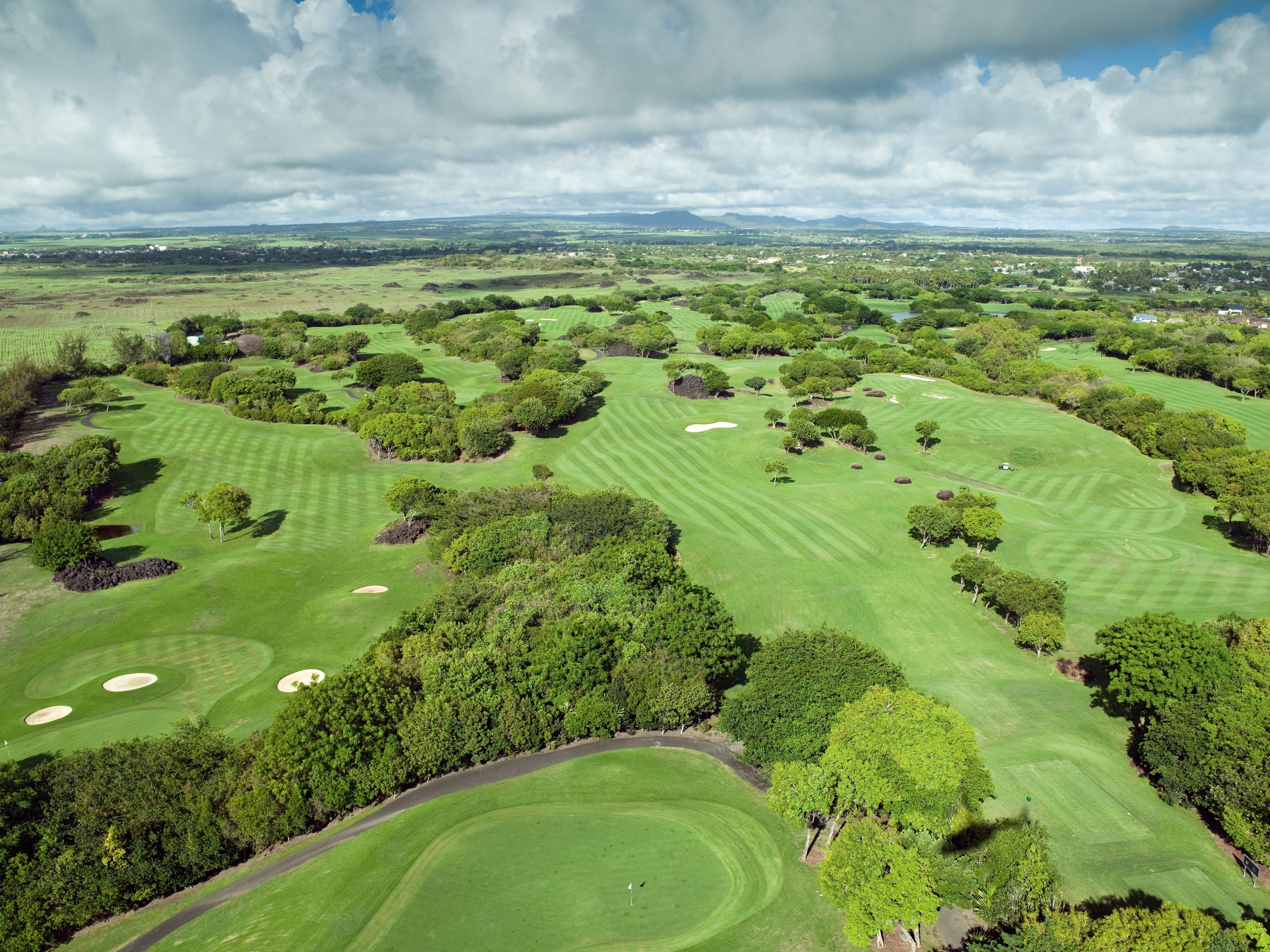 An aerial view of a golf course with multiple greens, sand bunkers, and a surrounding forest.