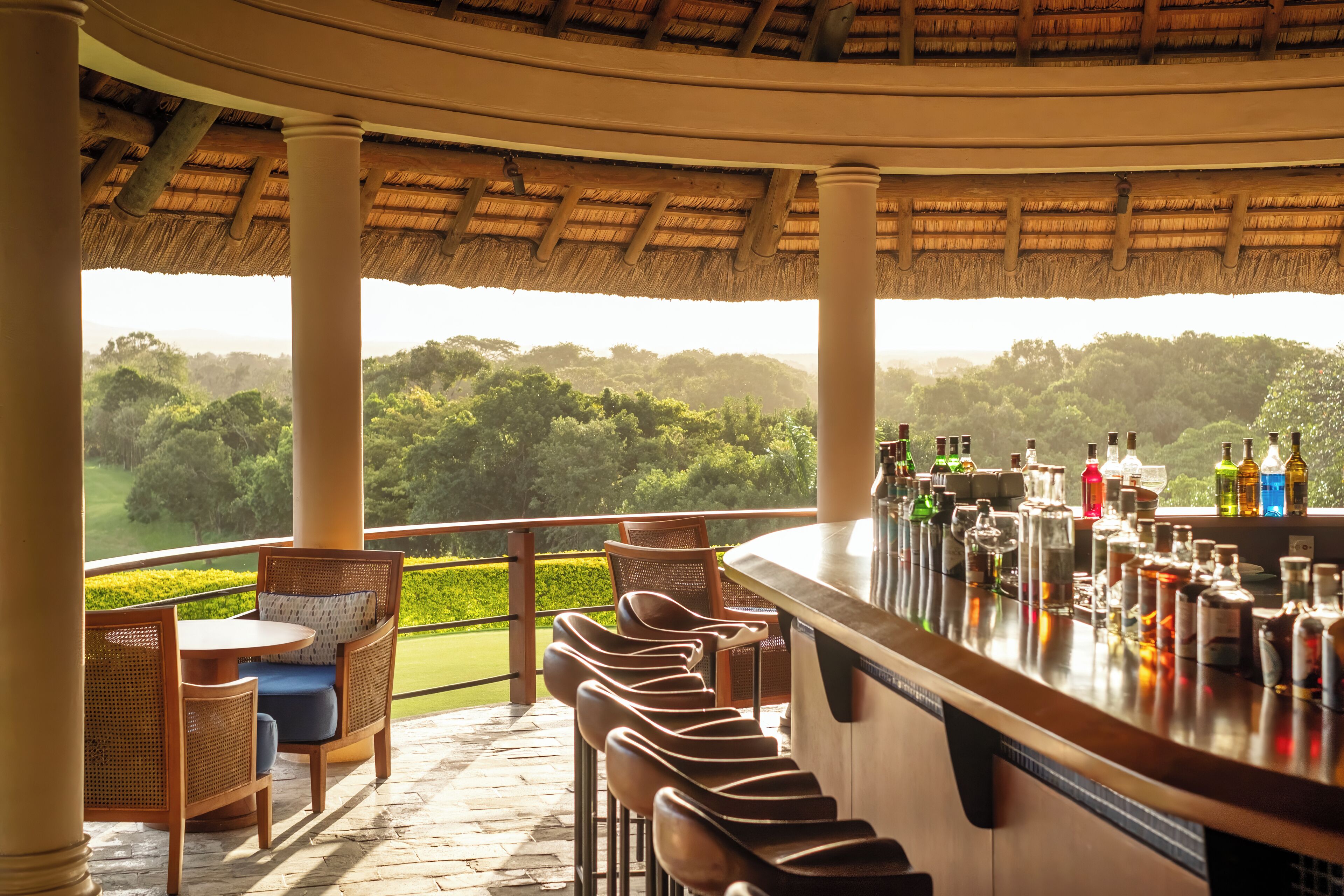 A bar area with a view of a lush landscape, featuring a thatched roof and wicker furniture.