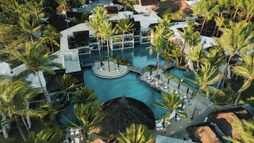 Oversigtsbillede af et resort med en central pool, omgivet af palmer og huse med stråtækte tage.