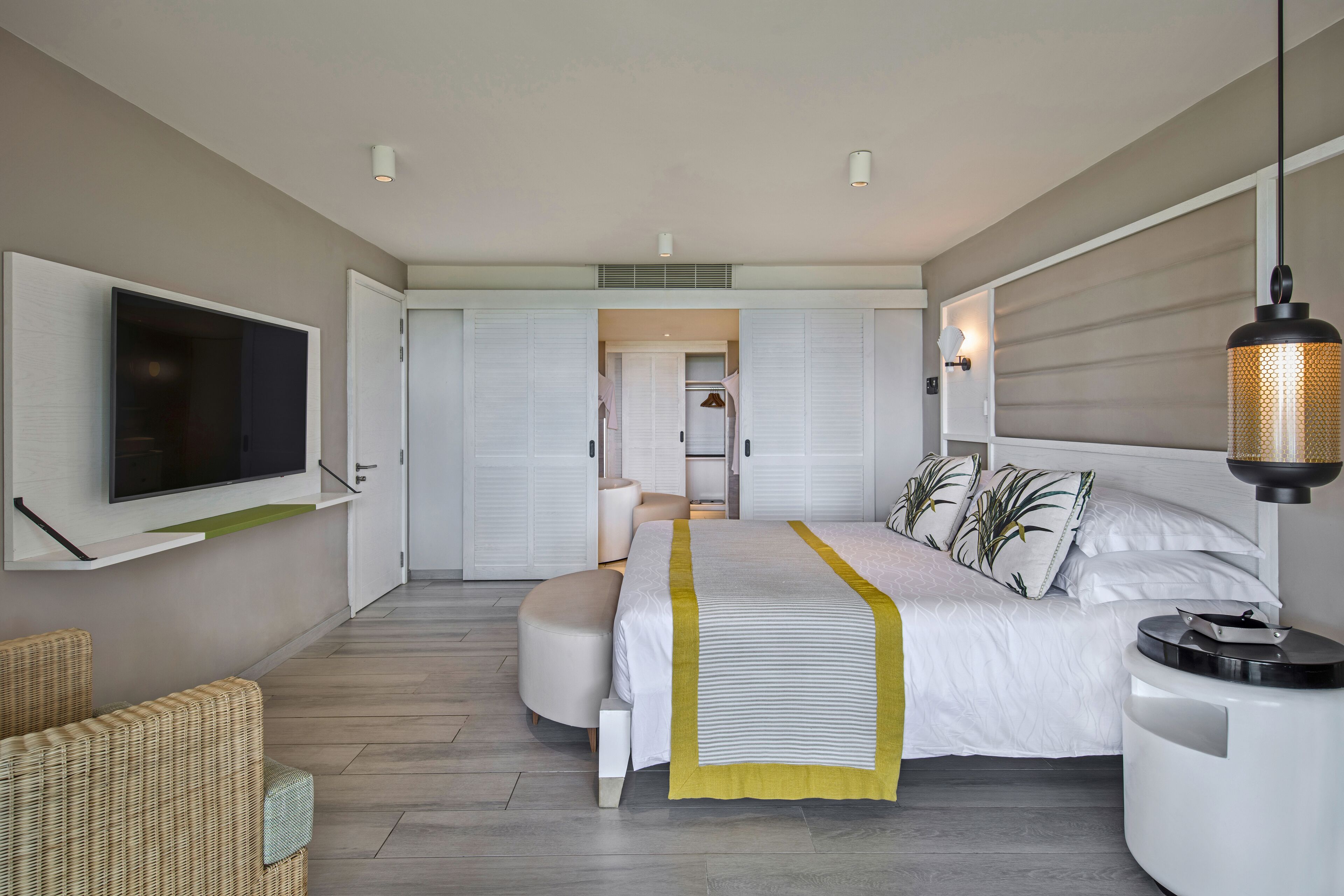 Un dormitorio moderno con una cama grande, un televisor montado en la pared, una mesita de noche y una lámpara colgante.