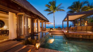 Relax by the serene infinity pool overlooking the ocean, surrounded by comfortable seating and a thatched-roof structure.
