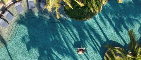Vista aérea de una piscina con agua azul cristalina, rodeada de palmeras y un sendero curvo.