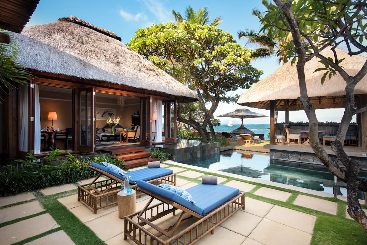 Un resort con piscina, sillones de descanso y un edificio con techo de paja.