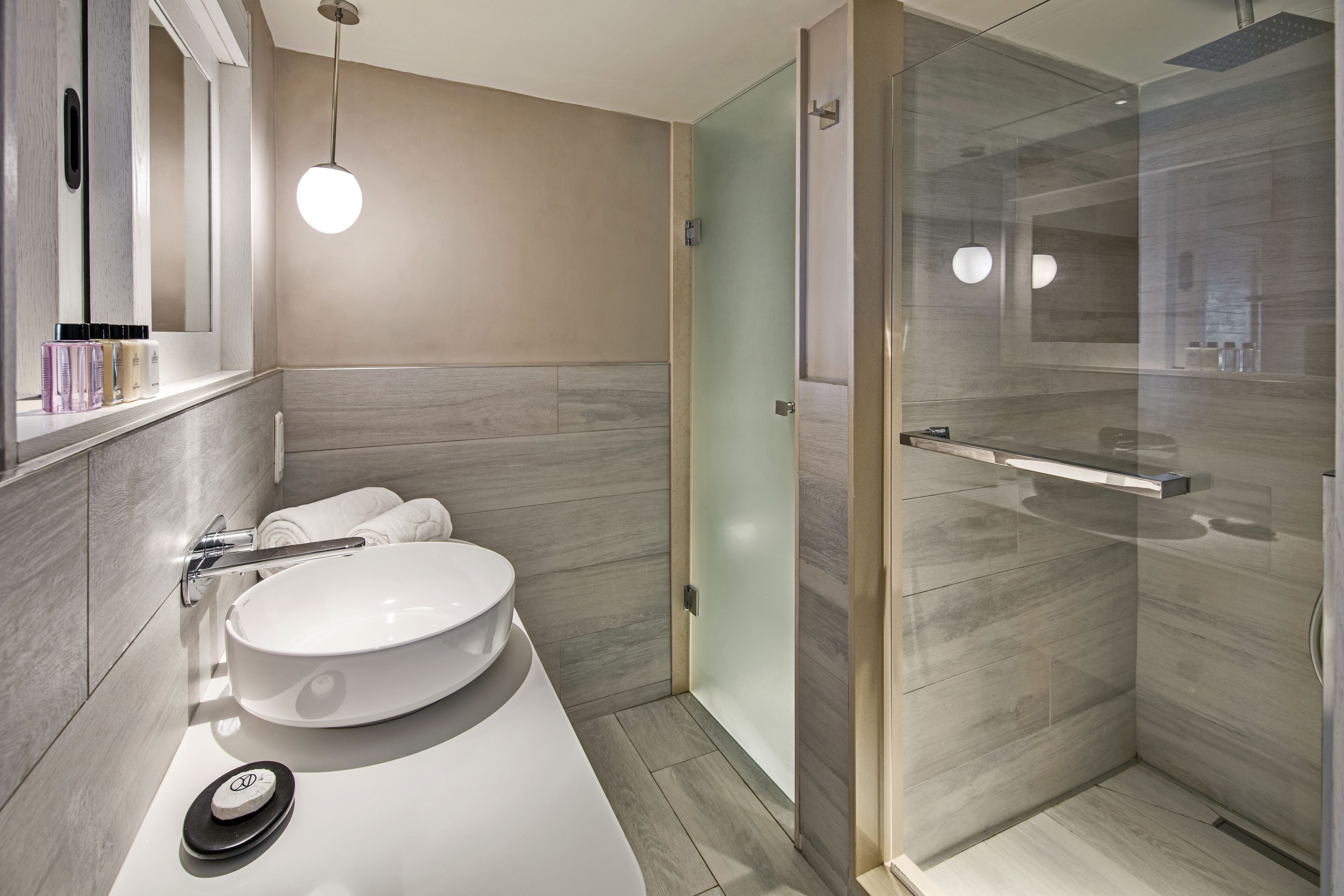 A modern bathroom with a large sink, a glass shower enclosure, and a mirror with a light fixture.