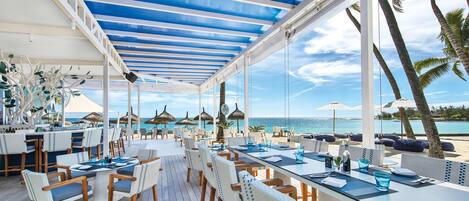 A covered outdoor dining area with tables and chairs, overlooking the sea.