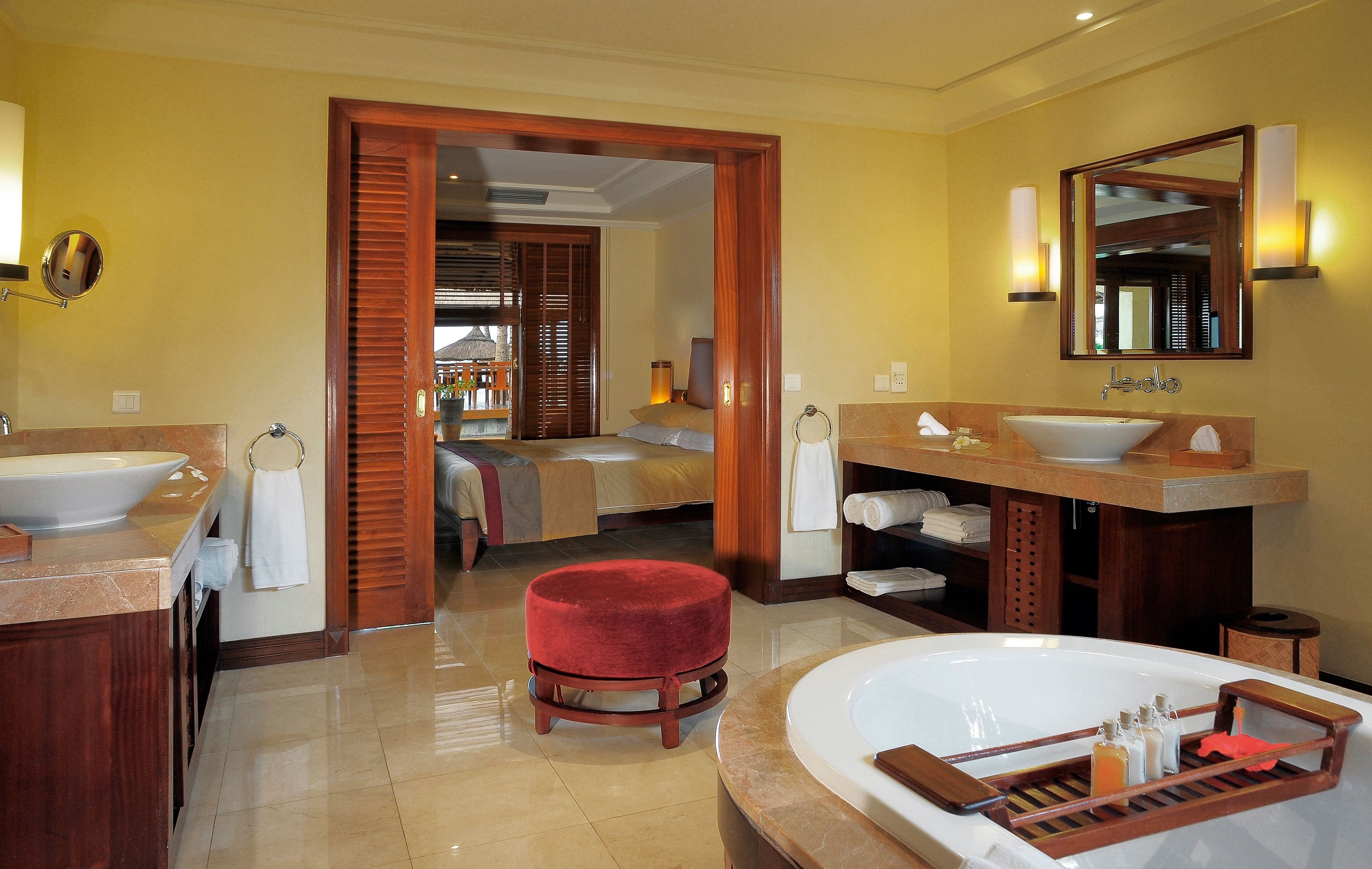 Un baño de hotel con una bañera grande, dos lavamanos, un reposapiés rojo y un espejo sobre el lavamanos.