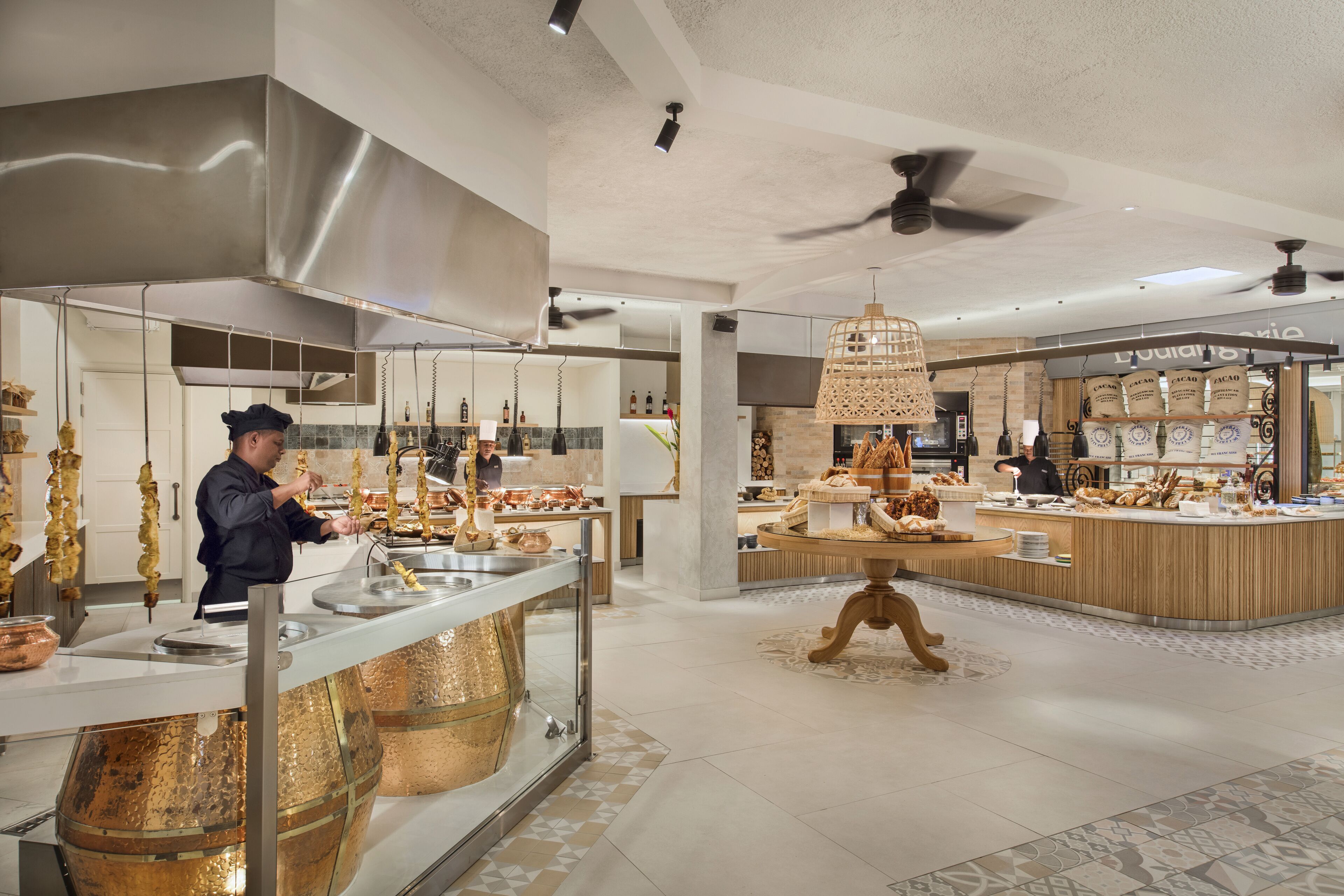 A modern kitchen area with stainless steel appliances, a chef preparing food, and a display of baked goods.