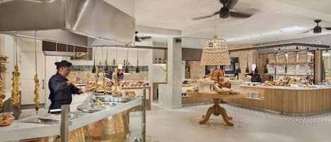 A modern kitchen area with stainless steel appliances, a chef preparing food, and a display of baked goods.