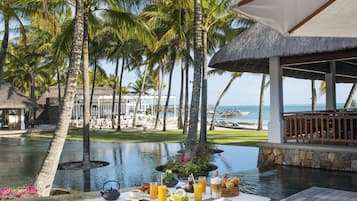 A dining table with chairs and a view of the ocean and palm trees.