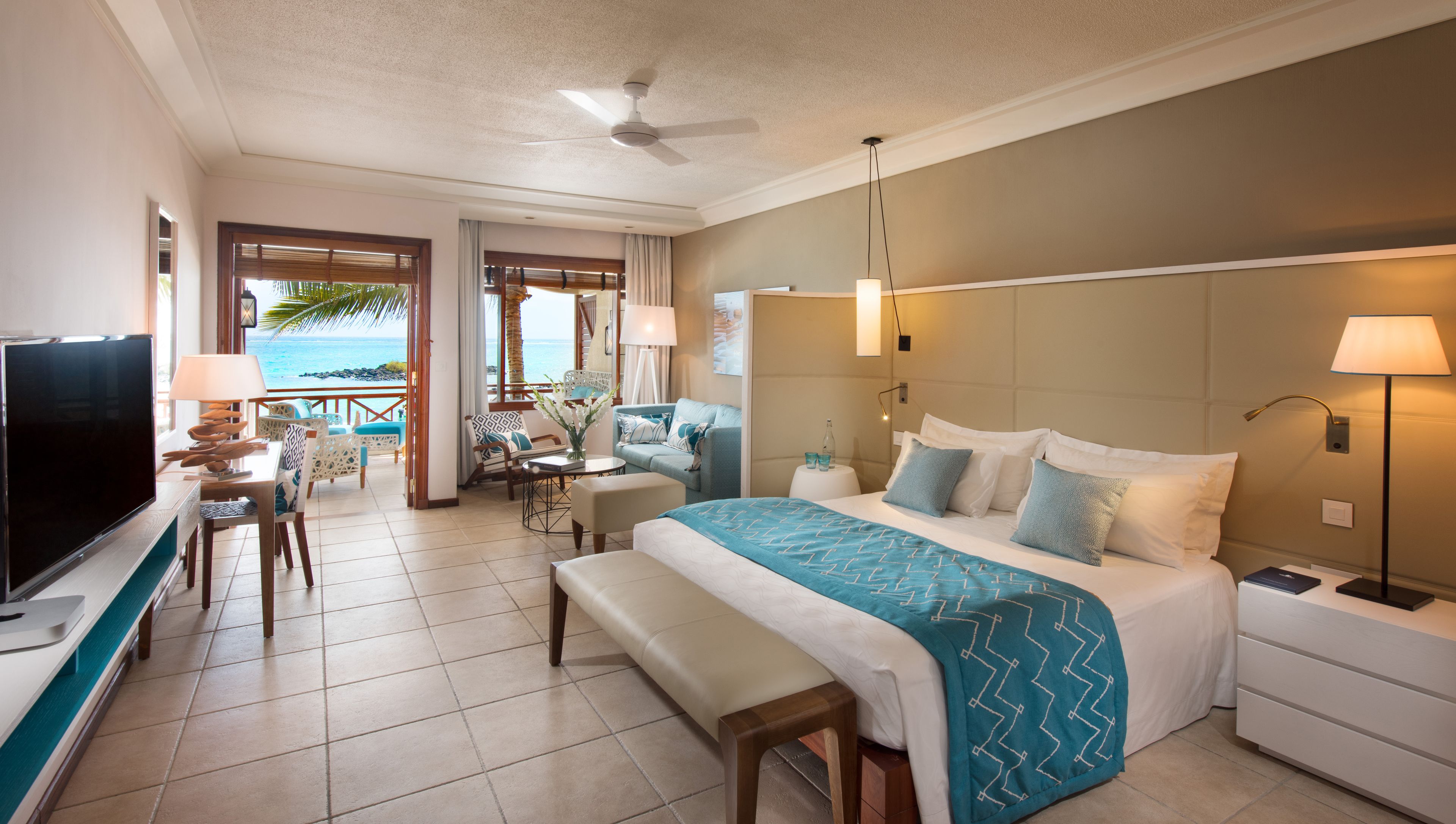 A hotel room with a bed, a TV, a desk, and a view of the ocean.
