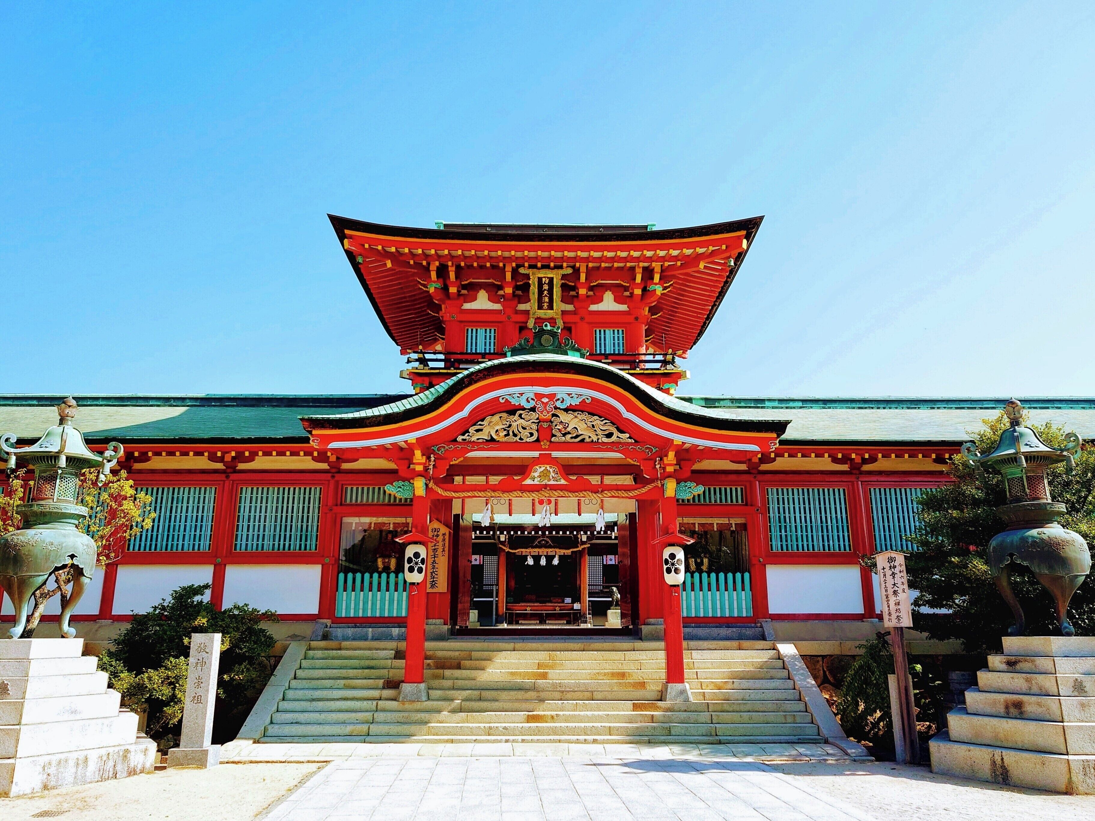 A traditional Japanese temple with a red and green roof, a central entrance, and a staircase leading up to it.