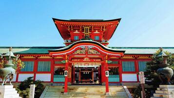 A traditional Japanese temple with a red and green roof, a central entrance, and a staircase leading up to it.
