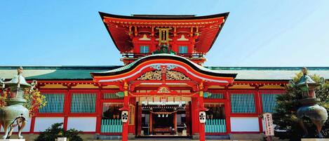 A traditional Japanese temple with a red and green roof, a central entrance, and a staircase leading up to it.