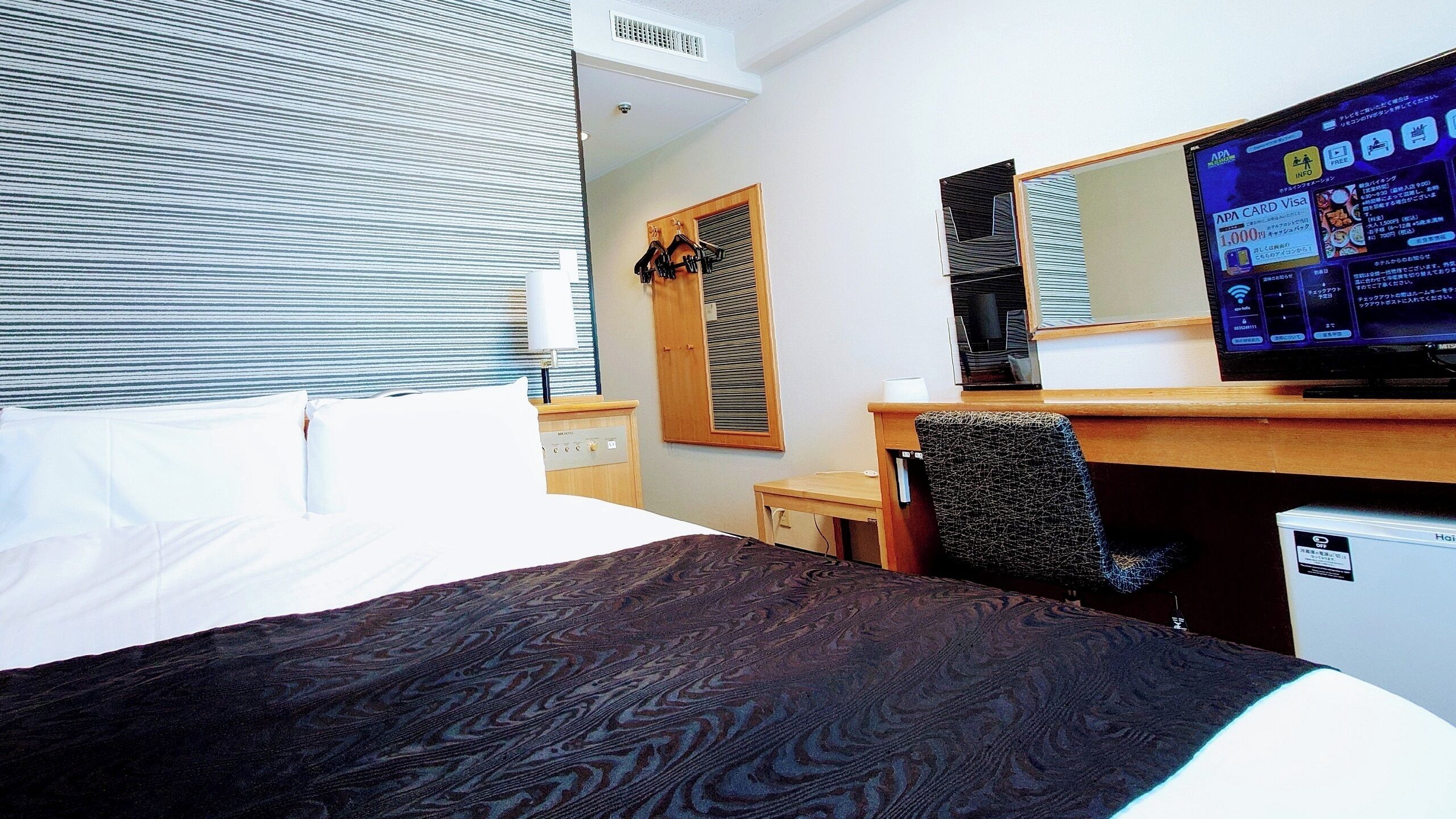 A hotel room with a bed, a desk, a chair, a television, and a window with blinds.