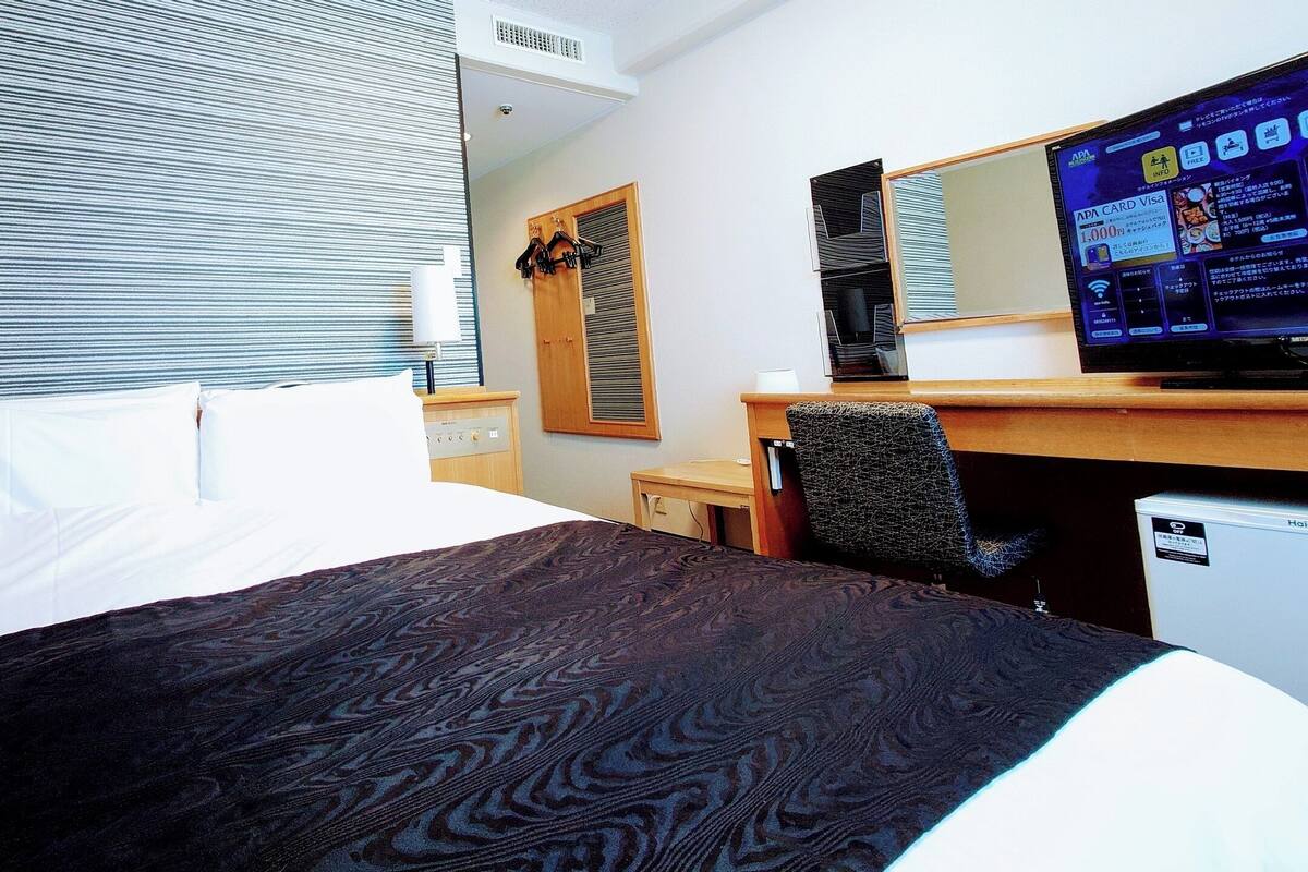 Ein Hotelzimmer mit Bett, Schreibtisch, Fernseher und einem Fenster mit Jalousien.