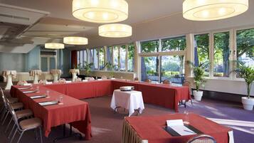 A conference room with multiple tables, chairs, and large windows providing natural light.