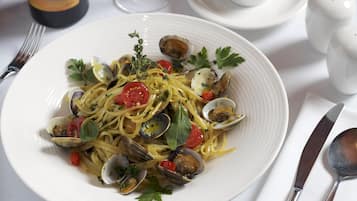 A plate of pasta with clams and vegetables, a wine glass, and salt and pepper shakers on a table.