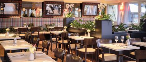 A restaurant with multiple tables and booths, each set with cutlery and a vase of flowers.