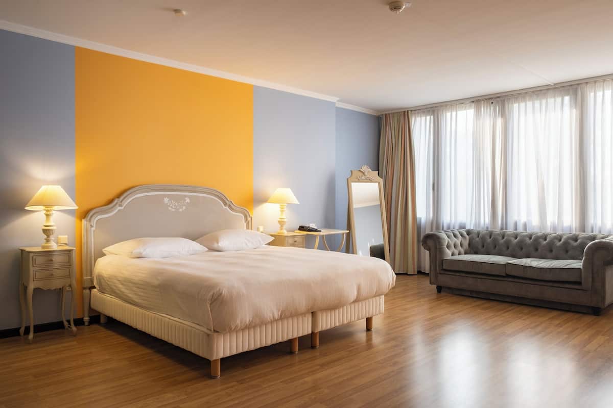 A hotel room with a bed, bedside tables, a sofa, and a large window with curtains.