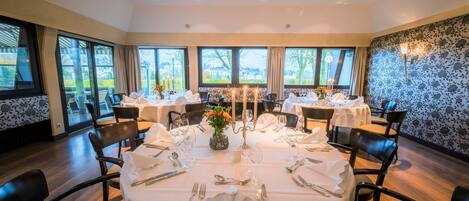 A dining area with round tables set for four, each with white tablecloths, silverware, and candles.