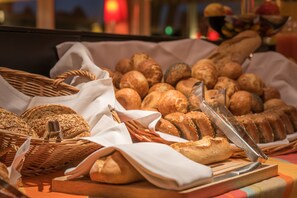 A variety of breads and pastries displayed on a table with a knife and tongs, suggesting a buffet or catering setup. - Hotel Parc Belle-Vue (Luxembourg City)