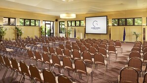 Un salón de conferencias con hileras de sillas, una pantalla de proyector y una bandera.