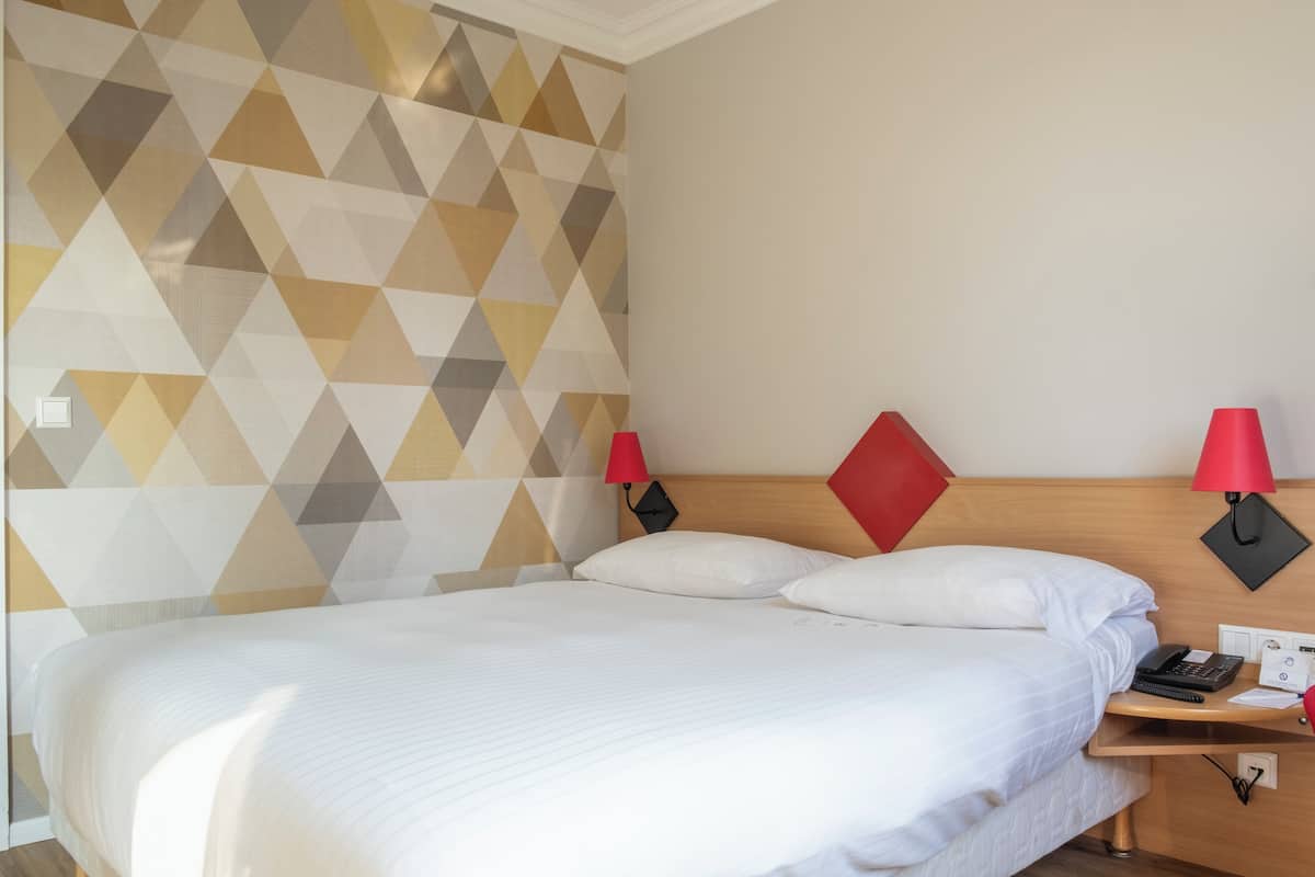 A neatly made bed with white linens, a wooden headboard, and two red wall lamps.