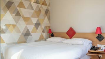 A neatly made bed with white linens, a wooden headboard, and two red wall lamps.
