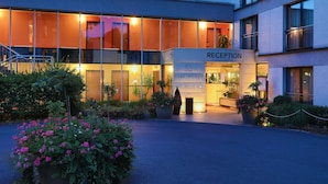 Una moderna recepción de hotel con fachada de vidrio, entrada acogedora y un jardín exterior bien cuidado.