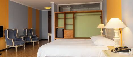 A hotel room with a bed, two armchairs, a desk with a lamp, a phone, and a wardrobe.