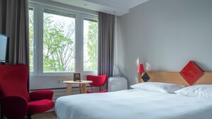 Una habitación de hotel con una cama grande, un sillón rojo, una mesita y un televisor.