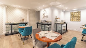 A modern dining area with a round table set for four, surrounded by teal chairs. - Hotel Riviera (Paris)