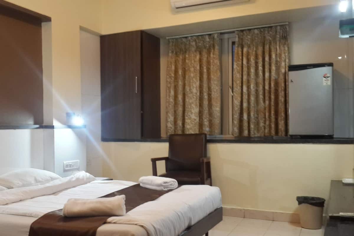 Una habitación de hotel con una cama, una silla, una ventana con cortinas y un refrigerador.