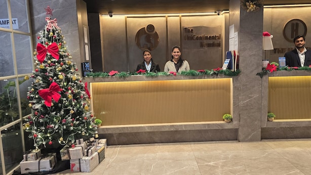 A reception desk with a Christmas tree and gifts, a sign reading "The Continental Mumbai," and a modern interior design. - The UniContinental - Campus Accommodation (Mumbai)
