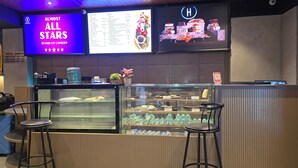 A hotel bar with a menu display, a coffee bar, and a glass display case with desserts. - The UniContinental - Campus Accommodation (Mumbai)
