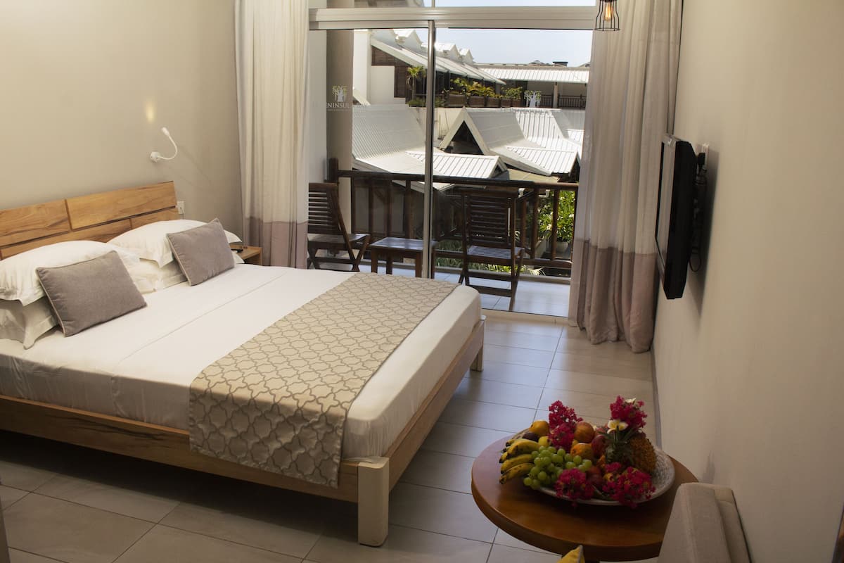 A hotel room with a bed, a dining area with chairs and a table, and a balcony with a view.