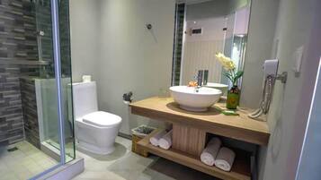 Un baño moderno con cabina de ducha de vidrio, inodoro blanco, tocador de madera con un espejo grande y un lavamanos.