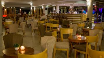 Un amplio comedor interior con varias mesas y sillas de madera, una zona de bar al fondo, y algunas personas cenando.