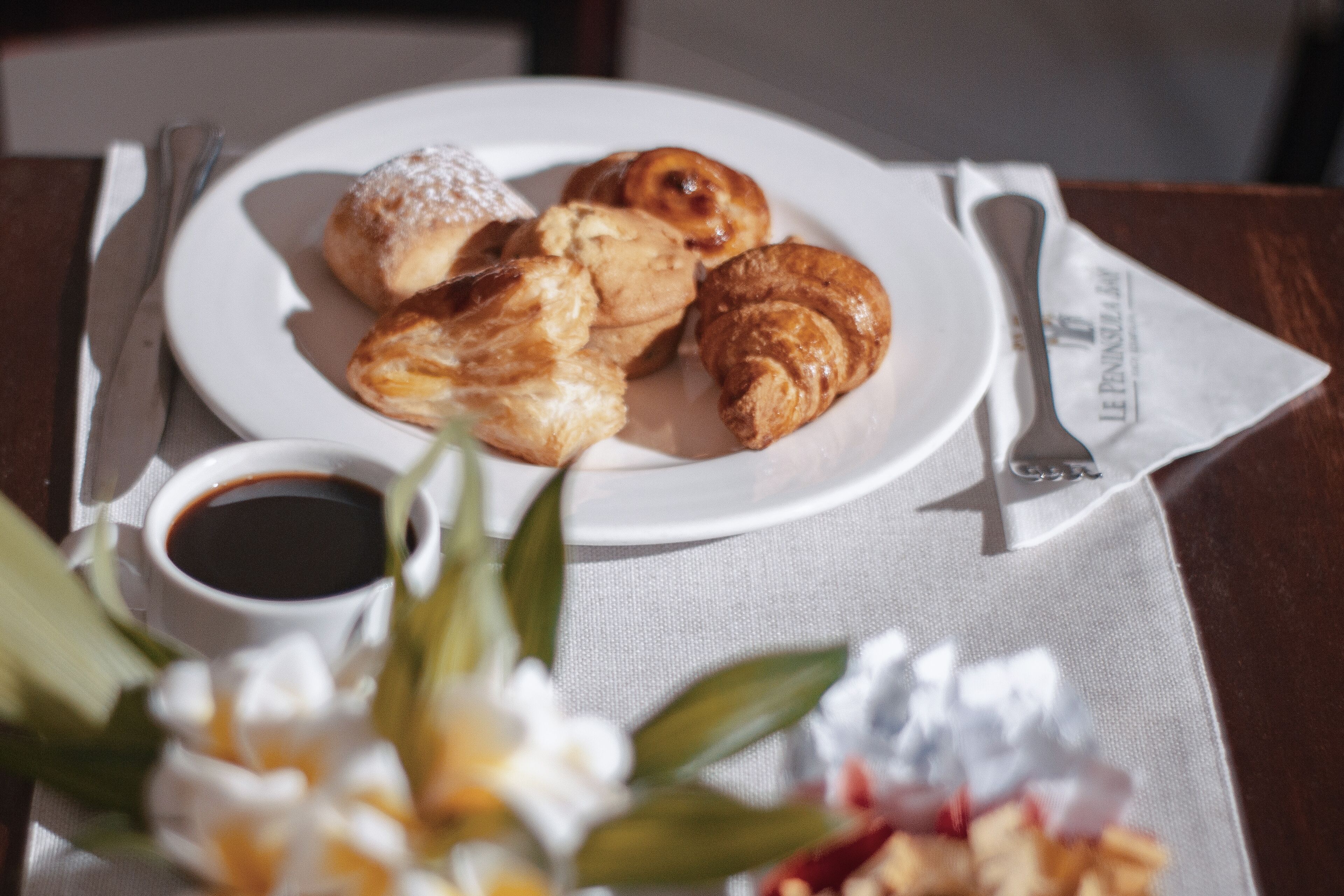 A plate of pastries and a cup of coffee on a table with a napkin and a spoon.