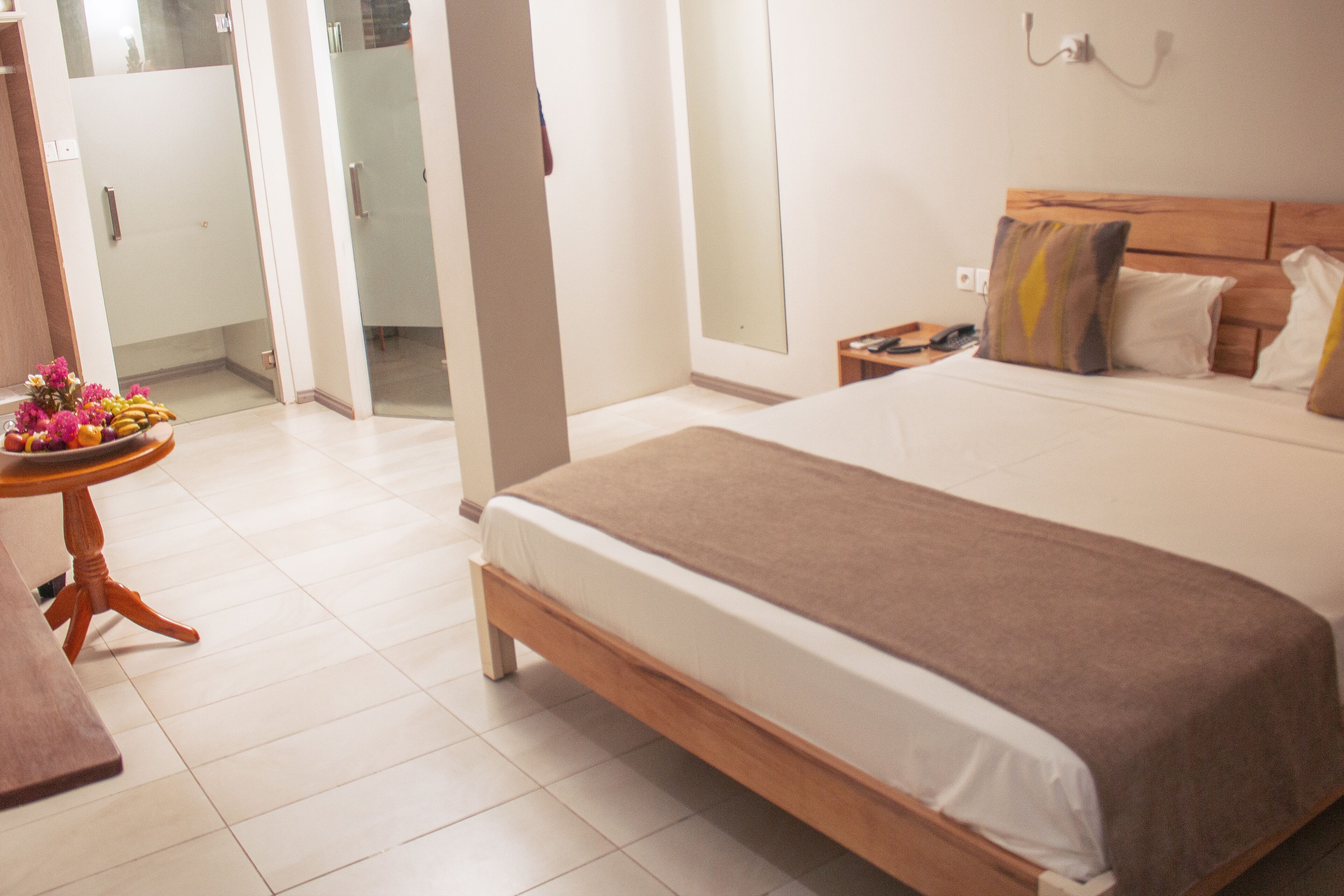 A hotel room with a large bed, a bedside table with a lamp, and a view of the hallway.