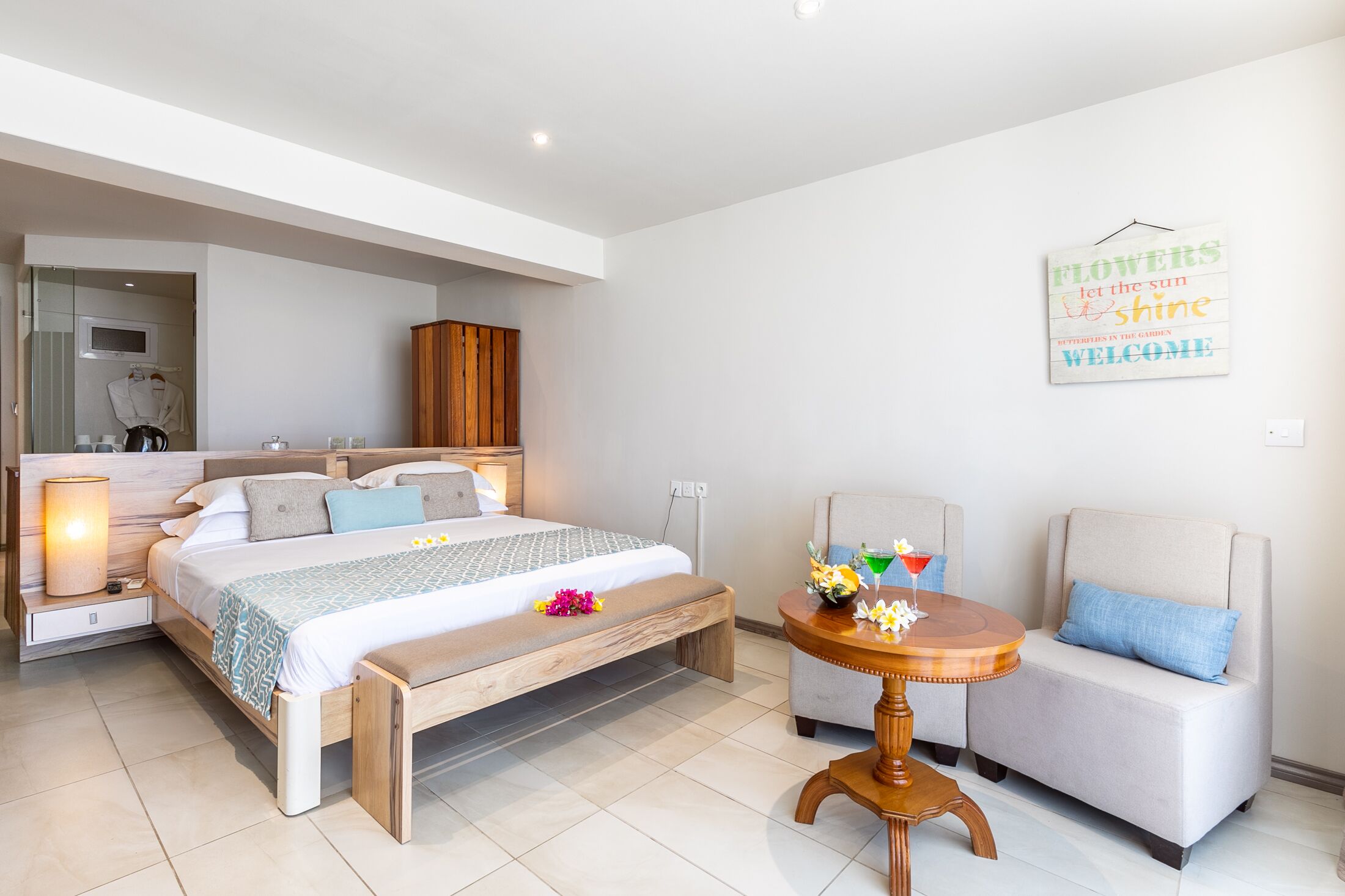 Un dormitorio moderno con una cama, mesita de noche, lámpara y una pequeña mesa redonda con flores.