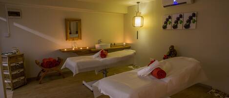 Een spa-ruimte met twee behandelbedden, een houten kast, een spiegel en een luchtverfrisser aan de muur.