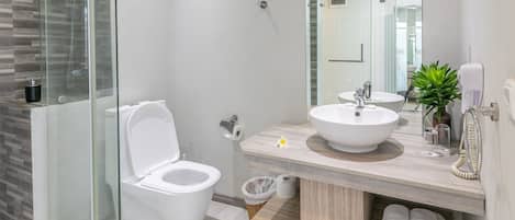 Un baño moderno con ducha envuelta en vidrio, inodoro blanco, lavamanos con espejo y perchero para toallas.
