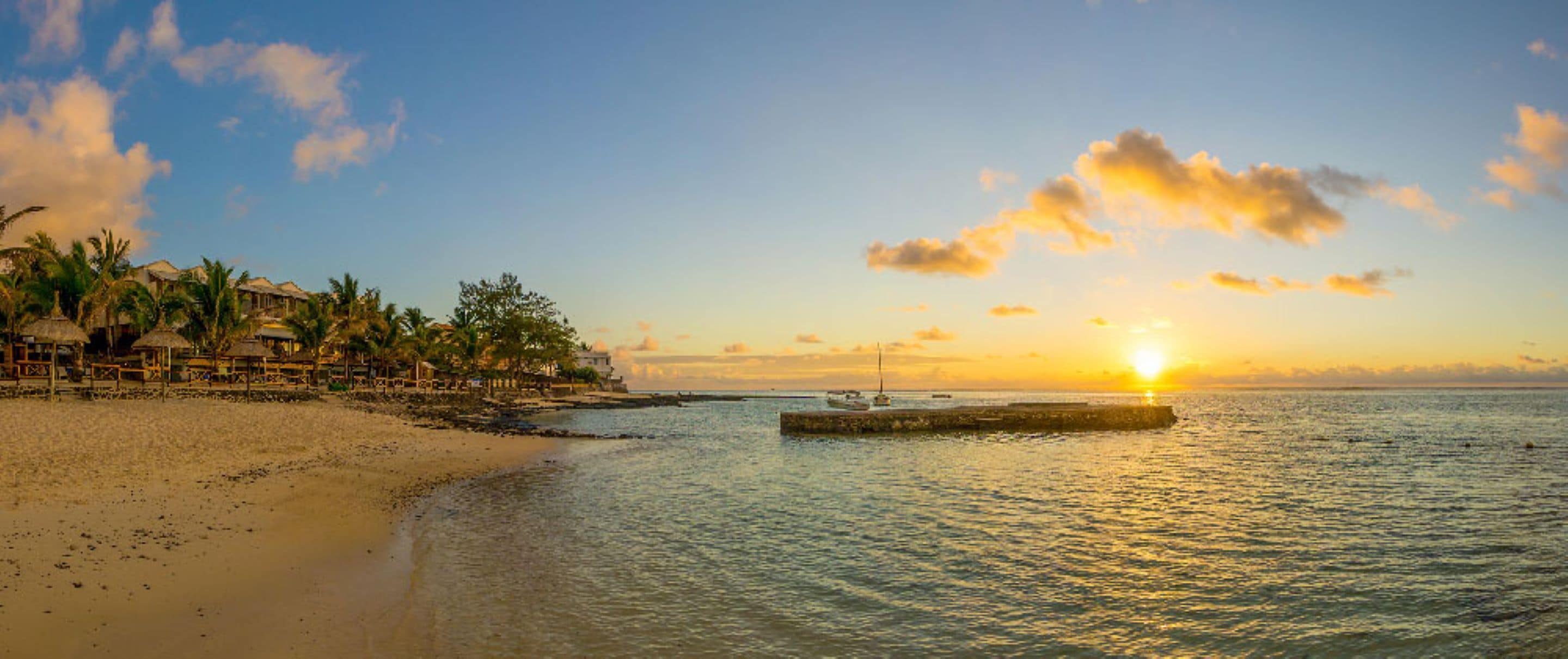 Une plage au coucher du soleil, avec des palmiers et un quai.