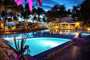 A swimming pool with lounge chairs and umbrellas, surrounded by palm trees and a covered seating area.