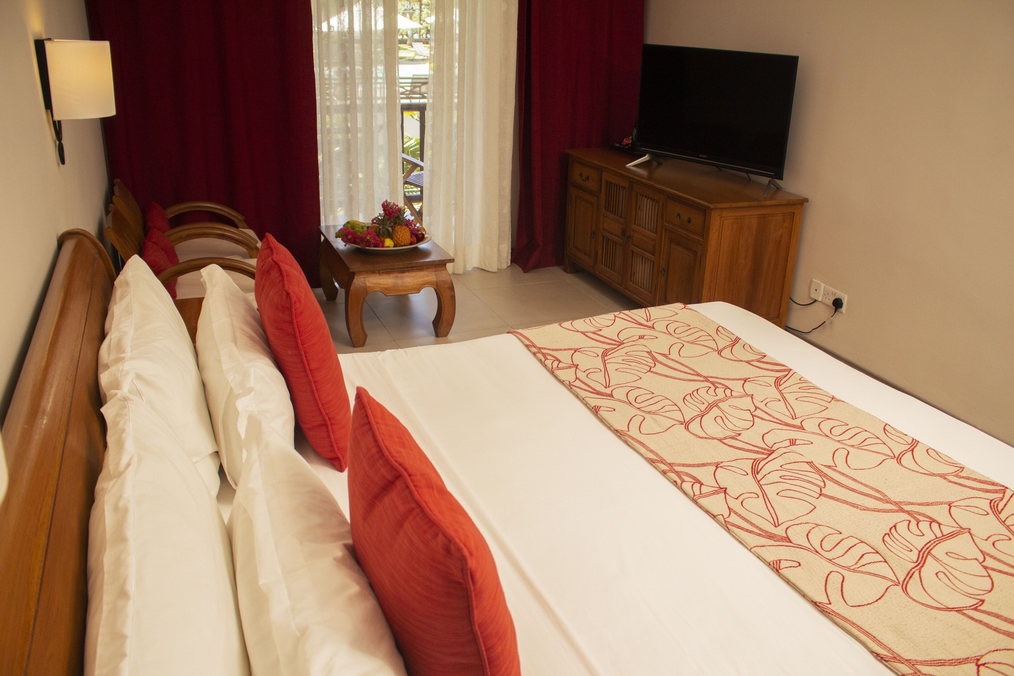 A hotel room with a large bed, a wooden headboard, a television on a wooden cabinet, and a small table with fruit.