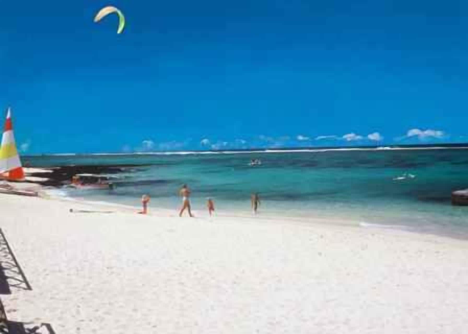 A beach with clear blue water, a lifeguard tower, and people walking along the shore.