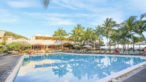 Piscina con sillas de descanso y palmeras, rodeada de edificios de un complejo turístico.
