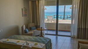 Habitación de hotel con cama, una pequeña mesa con un domo de cristal como centro y una silla, con vista al océano a través de un ventanal corredero.